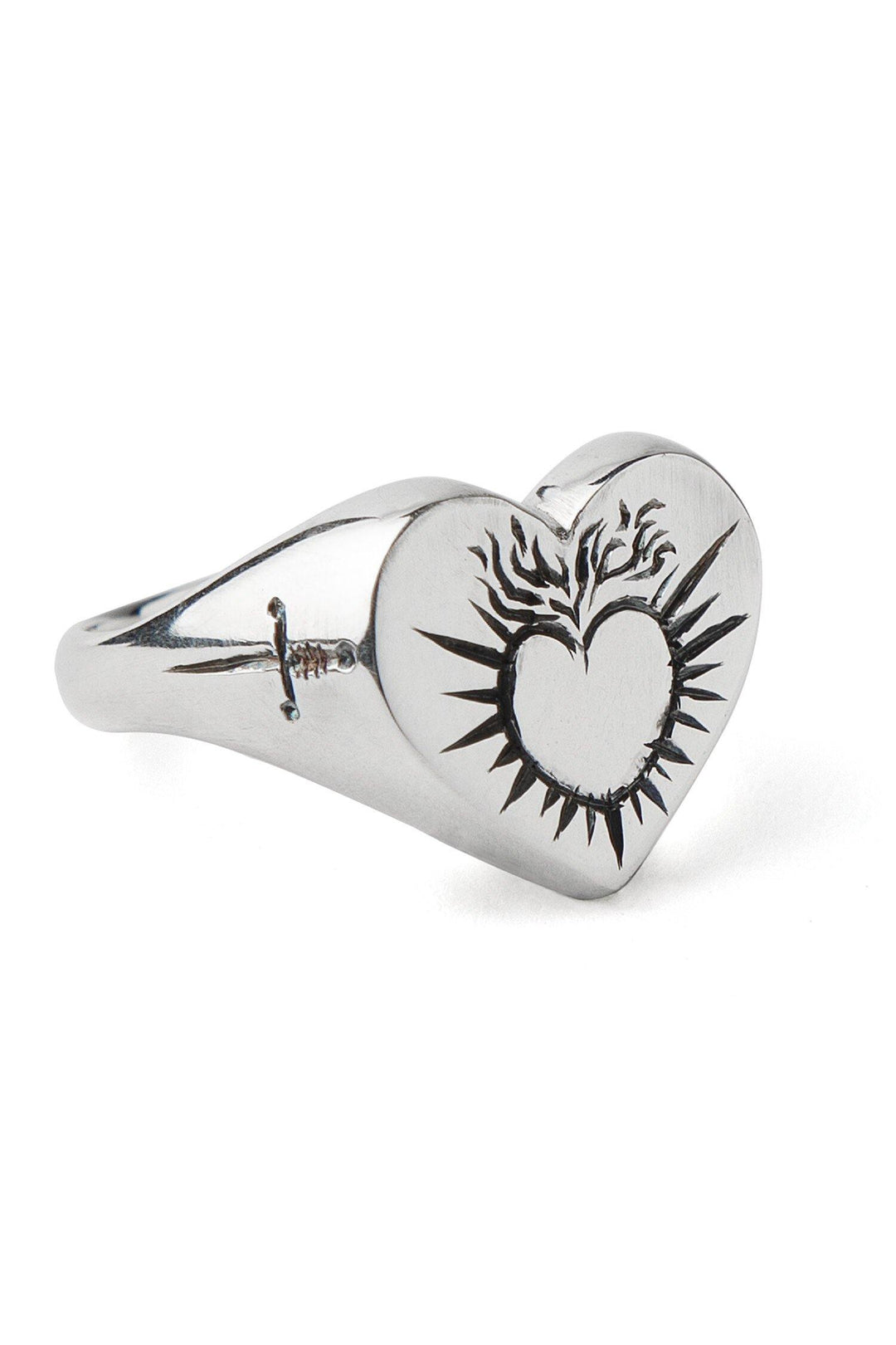 A handmade engraved ring in sterling silver, the **Sacred Heart Signet Ring by Cosmic Boulevard** features a heart-shaped top with a sacred heart surrounded by flames. The sleek, polished band also boasts a small engraving of a dagger.