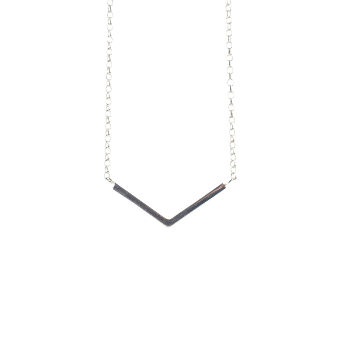 A minimalist necklace featuring a delicate sterling silver chain with a V-shaped pendant. The pendant consists of two slender metallic bars meeting at an angle to form an open chevron, creating a simple yet elegant design against a white background. The Sterling Silver V Necklace by Angela O'Keefe is the perfect accessory for any occasion.