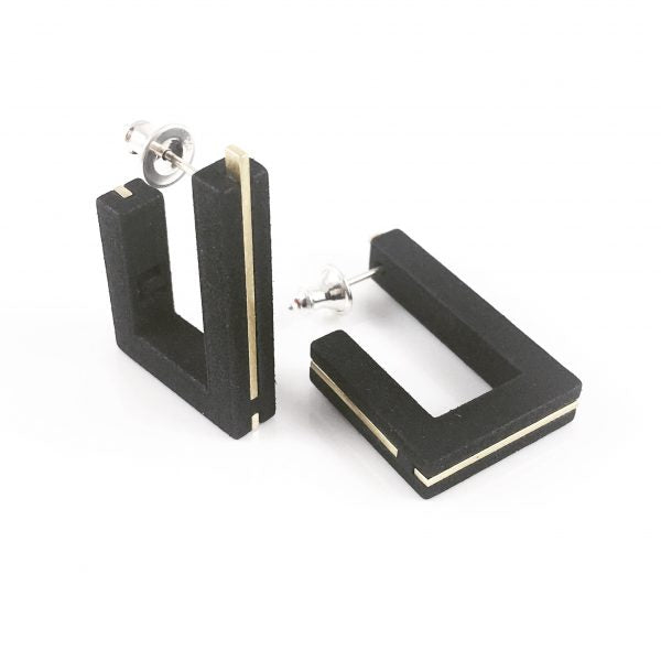A pair of Elsiem Vibe Brutalist Earrings in the shape of open rectangles with gold accents, reminiscent of Brutalist Architecture. Each earring has a silver post and back. One is standing upright, while the other lies down, showcasing both side and front views.