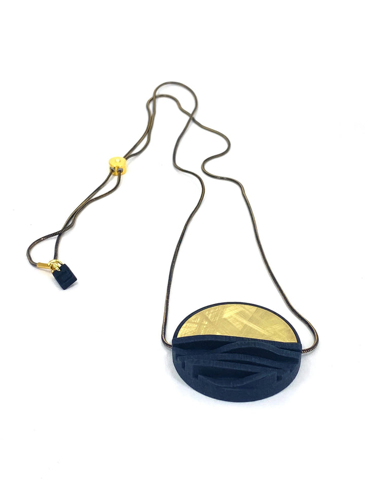 The Elsiem Vibe Wave Circle Fascia Necklace features a thin dark chain with an oval pendant—half dark blue with geometric patterns, half gold with textured detail—and a small gold bead, creating a striking black-and-gold accent.