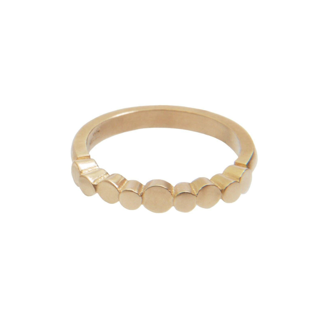 The Flow Pebble Ring 9ct Yellow Gold by Miriam Wade features a design of seven small, evenly spaced circular discs along the top half of the band. The rest of this Irish hallmarked ring is smooth and unadorned.
