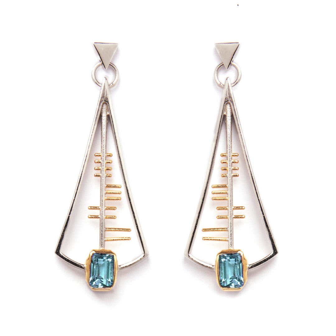 The Adeline Earrings by Gallardo & Blaine Designs feature a geometric, Art Deco-inspired design with a triangular sterling silver frame accented with gold and centered around a striking rectangular blue gemstone at the base. These earrings showcase a sleek, modern aesthetic with minimalist lines and shapes.