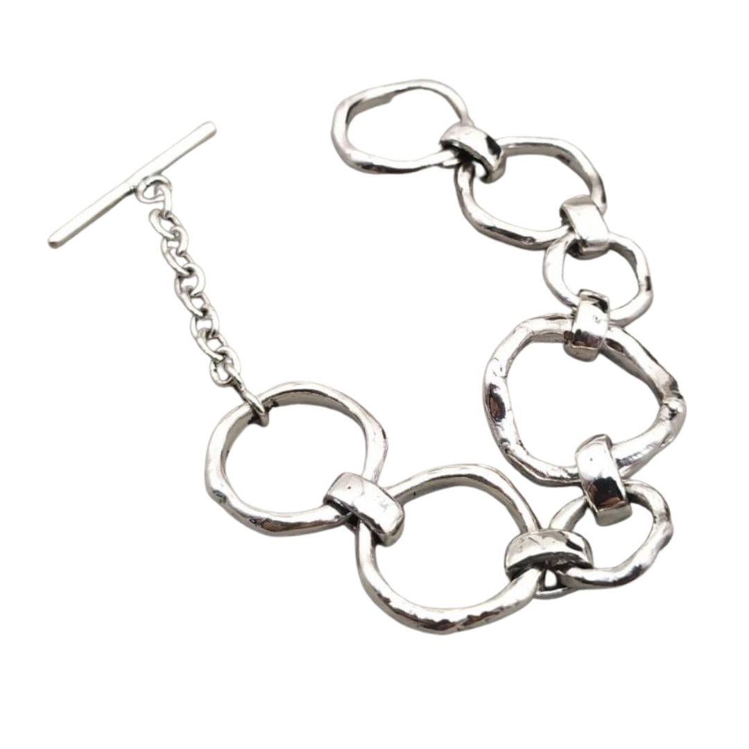 A stylish Sea Honey Bracelet Silver made of linked, thick silver rings is laid flat on a white background. It features a T-bar clasp with an adjustable chain, giving it a modern and elegant appearance. The metal has a slightly hammered texture, adding a touch of uniqueness to the new design by Gallardo & Blaine Designs.