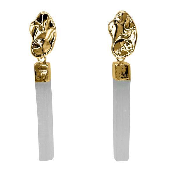 These Illusion Earrings by Aria V feature abstract, textured gold-tone metal at the top, with a square connecting a long, cylindrical white pendant handcrafted in Ireland. Using natural selenite stone, the overall design is both modern and elegant.