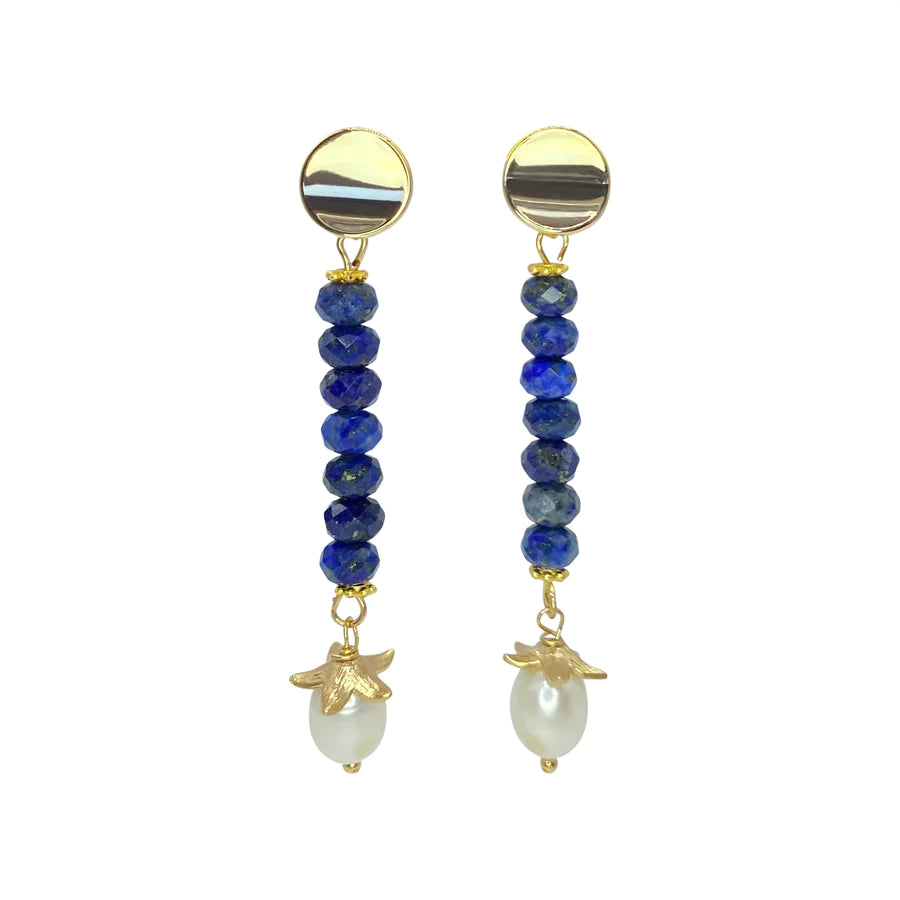 The Kaia Earrings by Aria V are a pair of handmade earrings featuring a 16k gold-colored circular stud, a vertical row of dark blue lapis lazuli beaded stones, and a white pearl drop with a small gold leaf accent at the bottom. The design is elegant and understated.