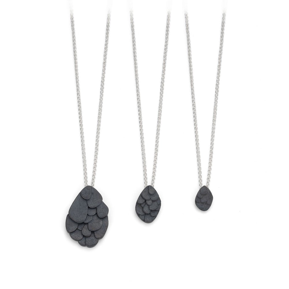 Three Leoma Drew Kimana Necklaces in Oxidised Silver, each featuring a dark, multi-layered, teardrop-shaped pendant of increasing size from right to left. The pendants have a textured, overlapping scale-like design. The background is white.