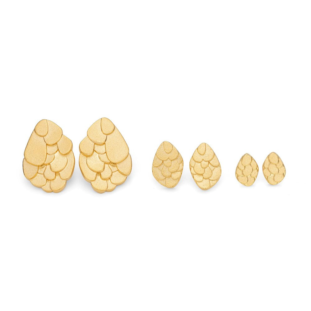 A set of six Leoma Drew Kimana Stud Earrings Gold, teardrop-shaped and frosted gold plated silver, arranged in a row. Each pair features a layered, scalloped design resembling fish scales. The earrings decrease in size from left to right.