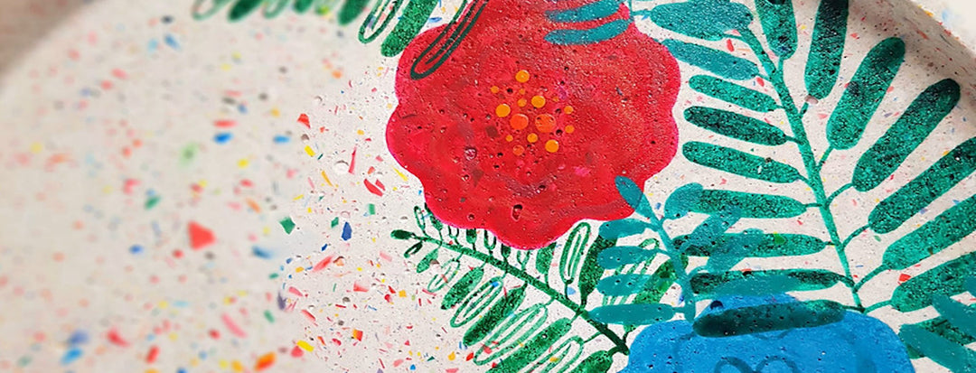 Close-up of a painted surface featuring a bright red flower, green leaves, and colorful speckles on a white, textured background.