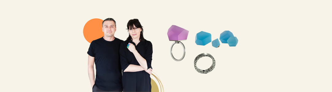 Two people in black shirts stand side by side, smiling, with colorful geometric rings and blue shapes displayed to their right on a light background with abstract orange and yellow circles.