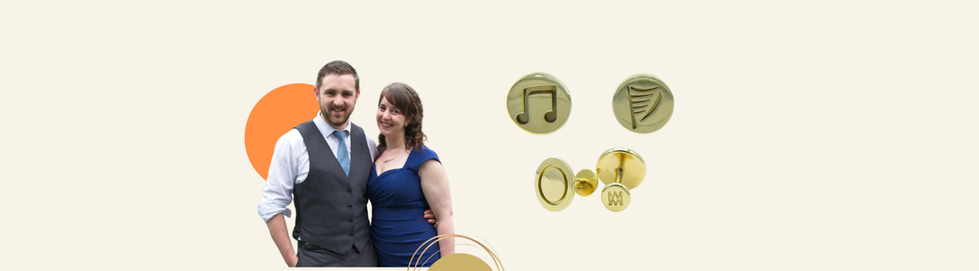A smiling couple stands together; the man wears a vest and tie, and the woman wears a blue dress. Next to them are three gold cufflinks, one with a music note, one with a harp, and one with initials.