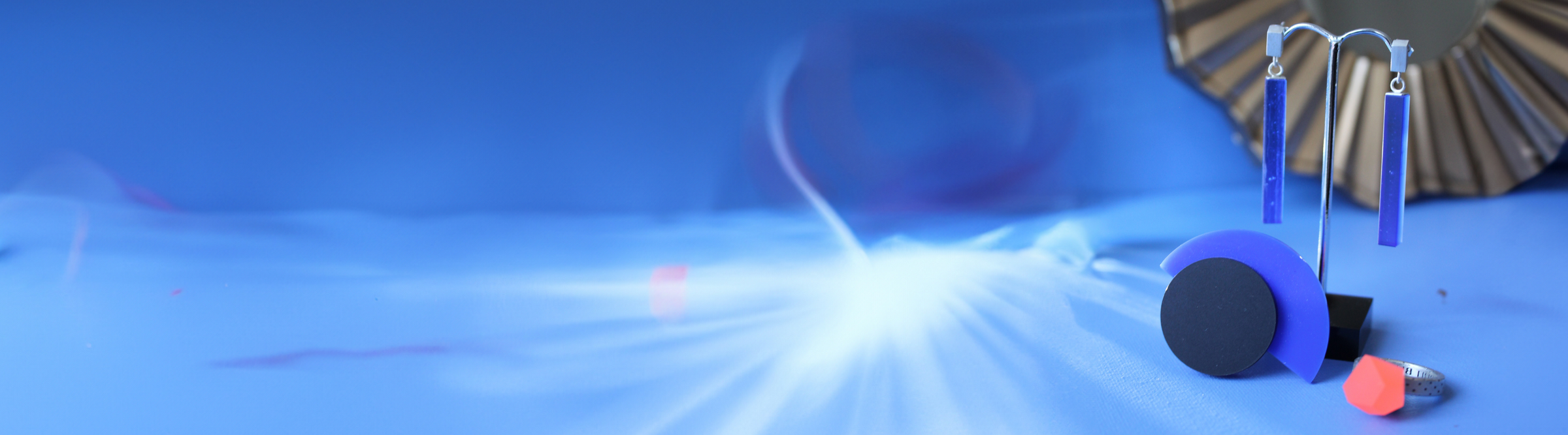 Abstract blue background with geometric shapes, including circles, rods, and a small orange triangle, with light streaks and a decorative mirror partially visible on the right side.