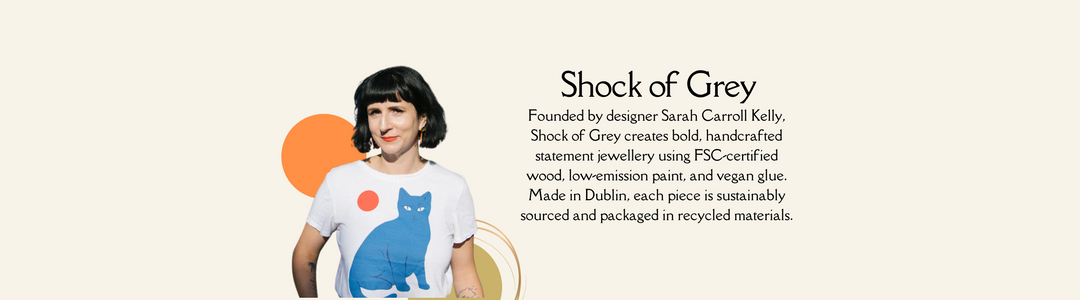 A woman with a black bob haircut wears a white t-shirt with a blue cat print. Next to her is text about Shock of Grey, a Dublin-based sustainable jewelry brand founded by Sarah Carroll Kelly.