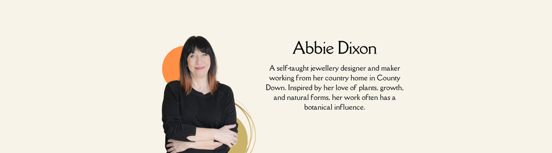 Image of a person with shoulder-length dark hair, wearing a black long-sleeved top, standing with arms crossed against a light background. The text reads: "Abbie Dixon, a self-taught jewellery designer, inspired by her love of plants and natural forms.