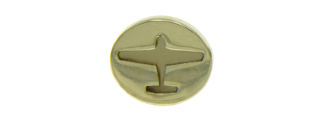 A circular gold pin with an embossed silhouette of an airplane in the center.