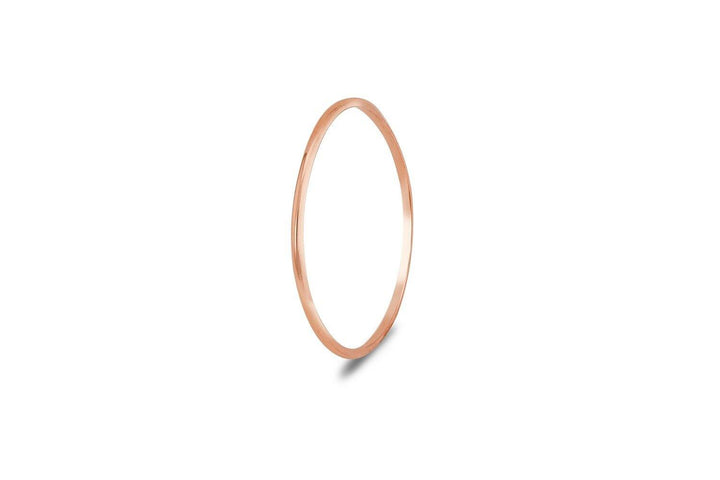 A thin, polished rose gold Cosmic Thread 9ct Gold Stacking Ring by Cosmic Boulevard is shown against a white background. The ring is simple and unadorned, highlighting its sleek and minimalist design. Crafted in a Dublin Studio, there is a subtle shadow beneath the ring, indicating its lightweight nature.