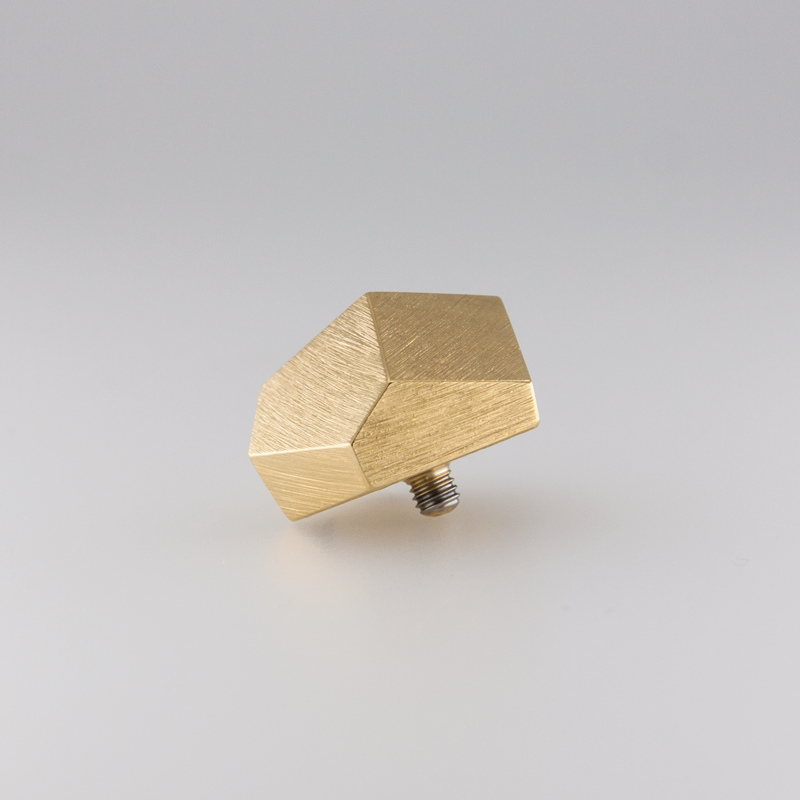 A gold-colored, geometric-shaped cabinet knob with a brushed texture against a gray background. Featuring a faceted design reminiscent of handmade jewellery, the Fruit Bijoux Fruit Bijoux Ring Top Goldrush has a screw attached at the base.