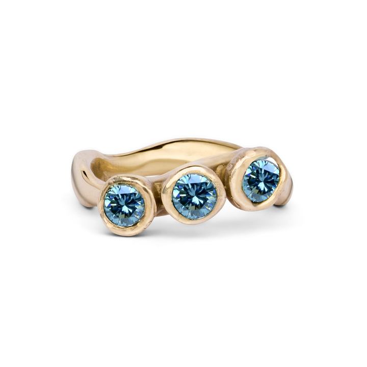 The Moonwater Ring by Madeleine Sculptural Jewellery is a handmade gold ring with three round blue gemstones in bezel settings on a wavy gold band—a unique piece of sustainable jewellery.