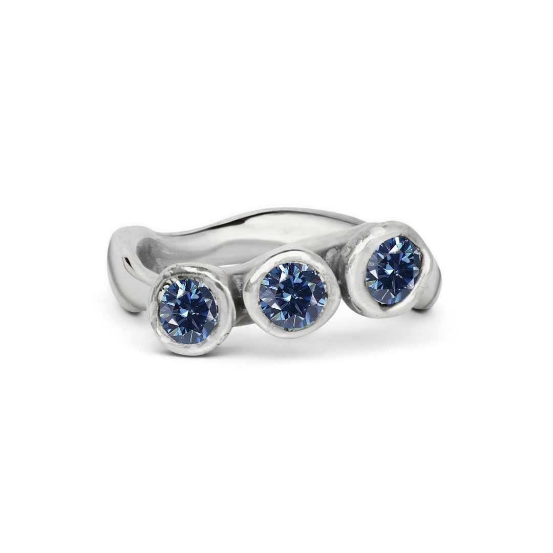 The Moonwater Ring by Madeleine Sculptural Jewellery is a silver ring with three round blue gems in individual bezels and a softly wavy band, inspired by hand-carved designs and crafted for sustainable jewellery lovers.