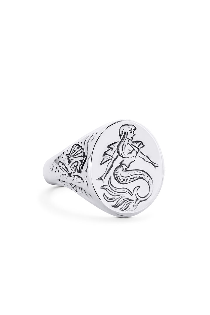 The Sterling Silver Siren Signet Ring by Cosmic Boulevard features a hand-engraved mermaid on the round face and detailed shell designs on the sides.