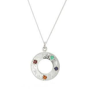 Cosmic Boulevard Shooting Star Rainbow Pendant Silver with a circular pendant adorned with multicolored gemstones in red, green, orange, purple, and clear. The pendant has a textured design and a hollow center resembling shooting stars, handmade in Dublin. It hangs from a delicate sterling silver chain.