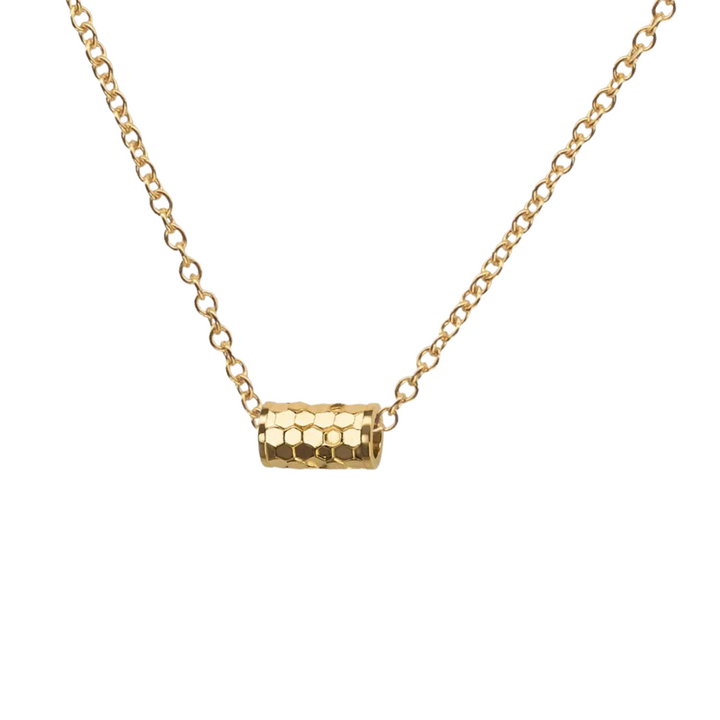 A Tiny Karma Wheel Necklace Gold with a delicate 18kt gold filled chain from Andrea Mears Jewellery features a cylindrical pendant with a honeycomb pattern. The pendant is centered on the chain, adding a modern and stylish touch to the accessory.