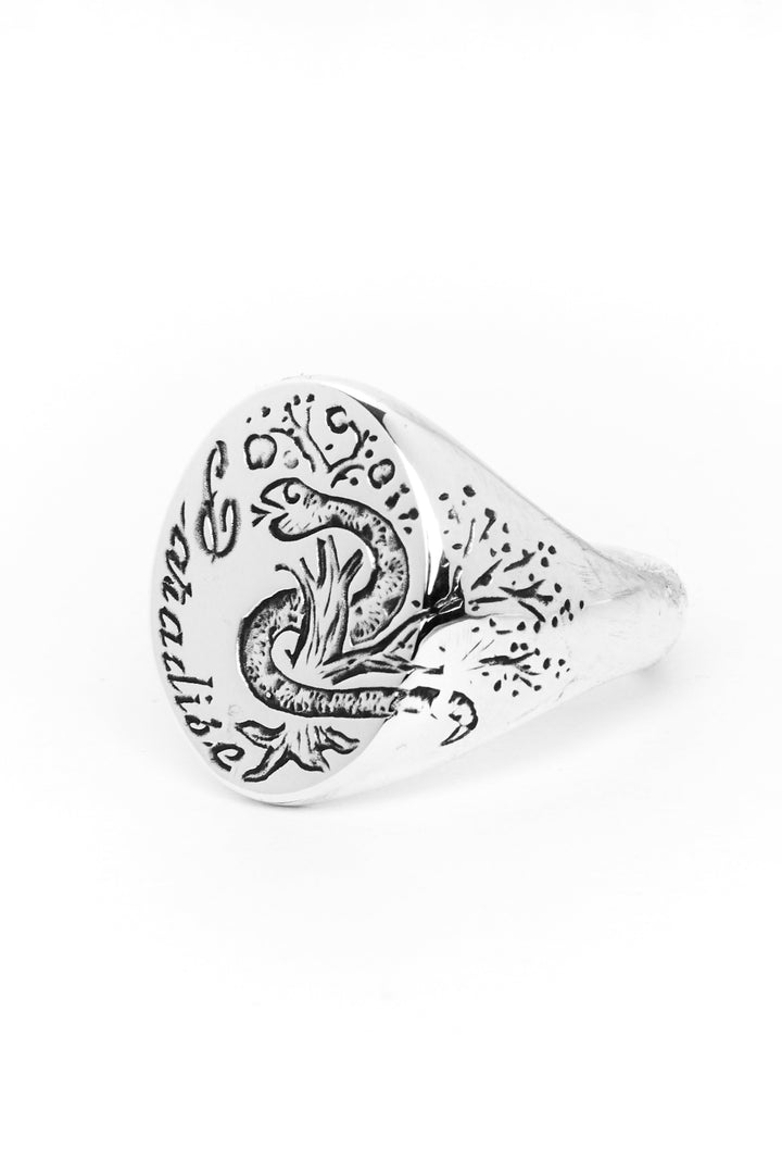 The Cosmic Boulevard Sterling Silver Paradise Signet Ring features a circular face adorned with an intricate lizard design. The hand-engraved lizard and surrounding patterns add detailed texture, while the ring showcases a smooth, polished band contrasting with the ornate face.