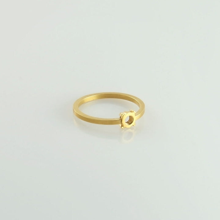 A minimalist 24ct gold-plated ring with a small, gear-shaped embellishment on top, placed on a plain white background. The Fruit Bijoux Minimal Ring Gold Plate adds a unique touch to its brushed finish.