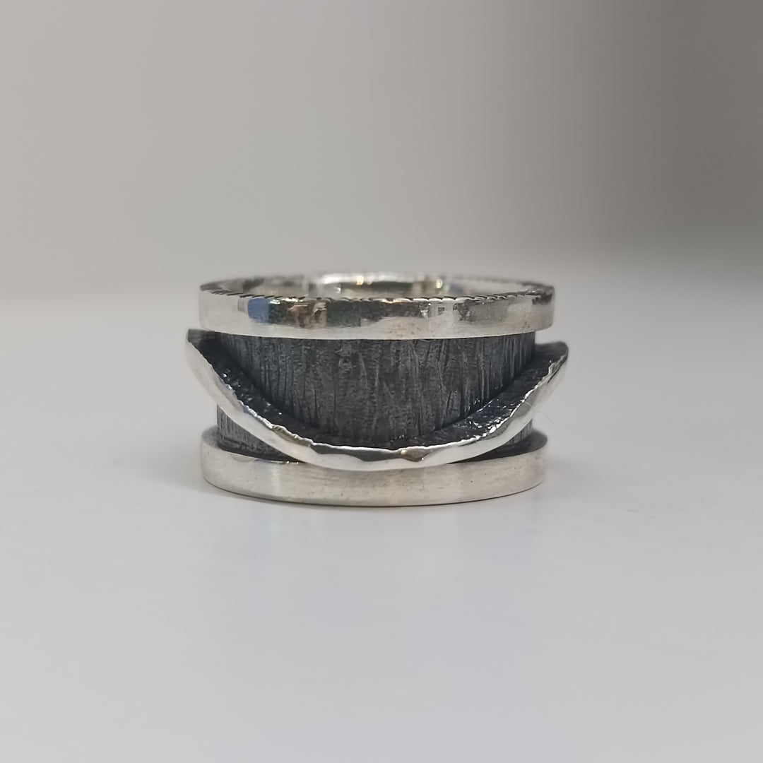 The K.And Wave Spinner Ring features a handcrafted textured sterling silver band with a wavy, polished edge and oxidised finish. This unique ring wraps partially around the center and is displayed on a plain white surface with a blurred background.