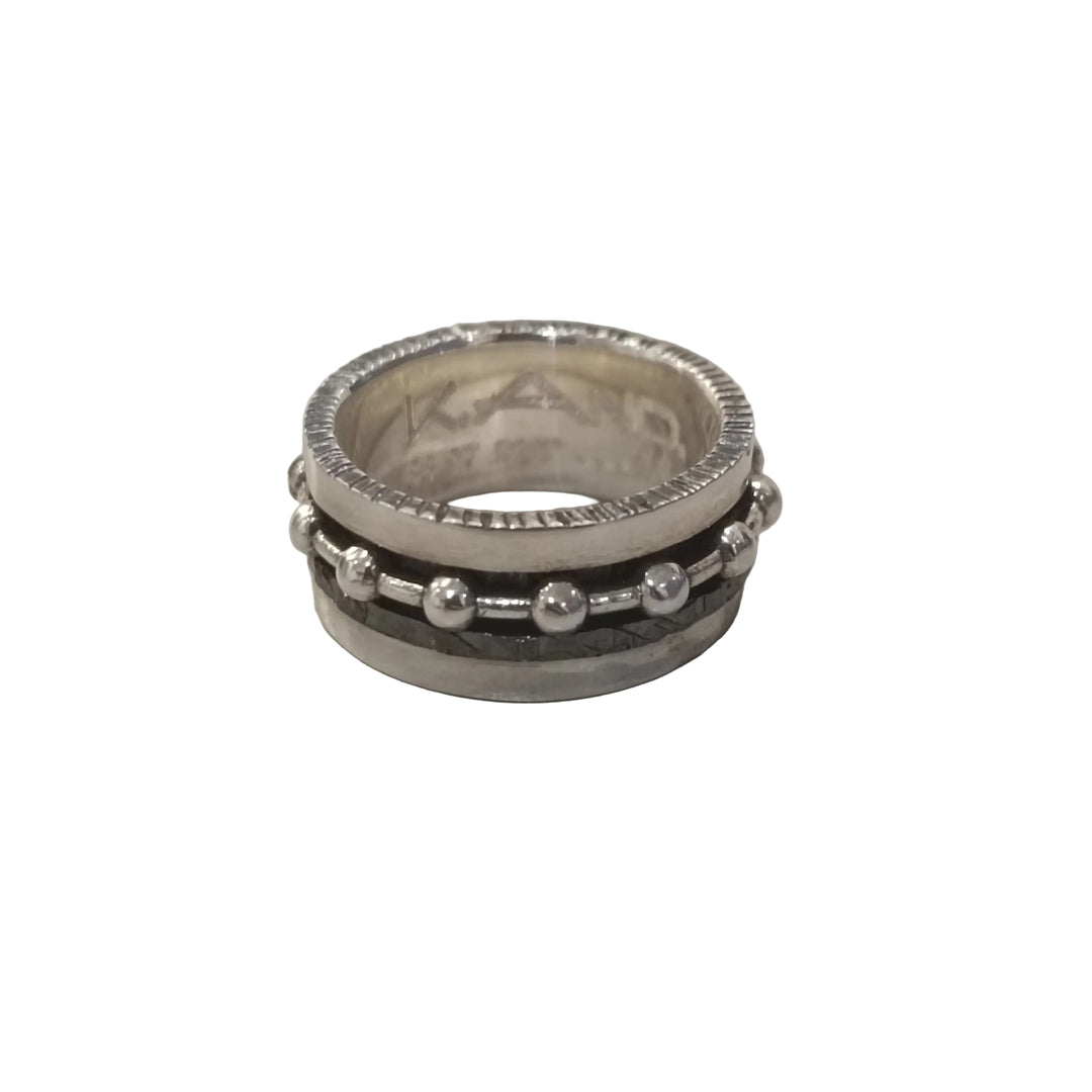The K.And Silver Double Spinner Ring with Balls stands upright on a flat, light surface, showcasing its textured edge and two outer bands—one smooth, the other decorated with small round balls.