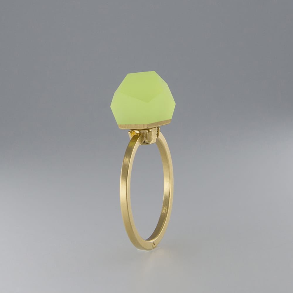 A Fruit Bijoux Fruit Bijoux Ring Top VU Crystals Neon Yellow with a large, faceted, pale green gemstone set in a minimalist design. The background is a smooth gradient of gray tones, highlighting the ring's elegant simplicity.