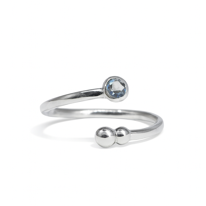 The Bauble & Stone Ring by Watermelon Tropical is a minimalist silver open band with a round blue quartz on one end and two small silver beads on the other, shown on a white background—ideal for handmade jewellery lovers.