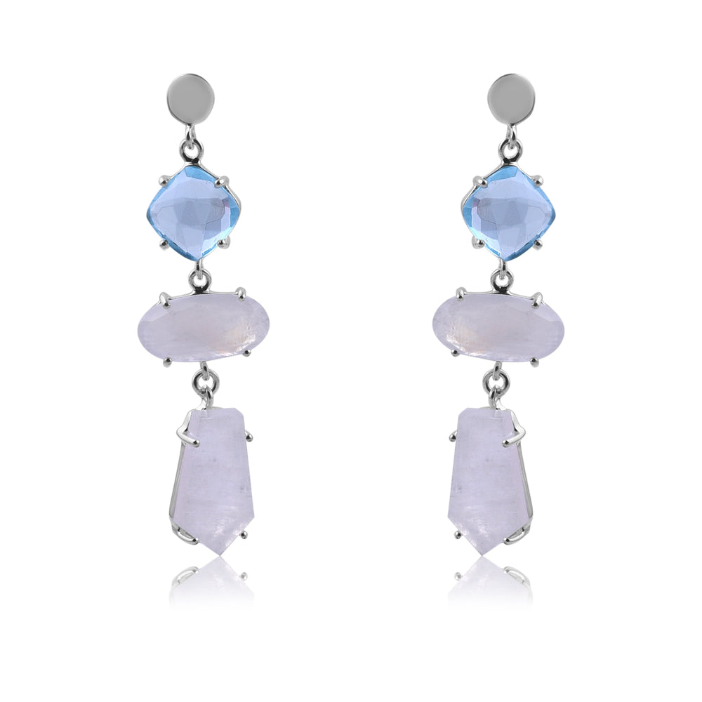 A pair of elegant Moonstone & Blue Quartz Silver Drop Earrings by Watermelon Tropical featuring a blue gemstone at the top, followed by a light purple oval stone in the middle, and a light purple geometric-shaped stone at the bottom. The earrings have a reflective, polished finish.