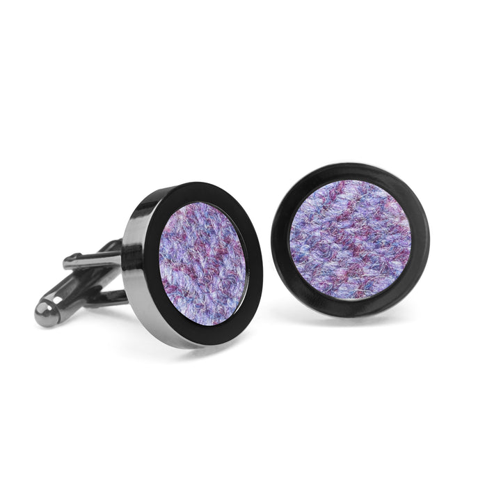 A pair of Iris Tweed Cufflinks by Orwell & Browne with black edges and a textured purple and blue fabric inlay, reminiscent of Donegal tweed cufflinks. The cufflinks are angled, one lying flat and the other standing upright, both against a white background.