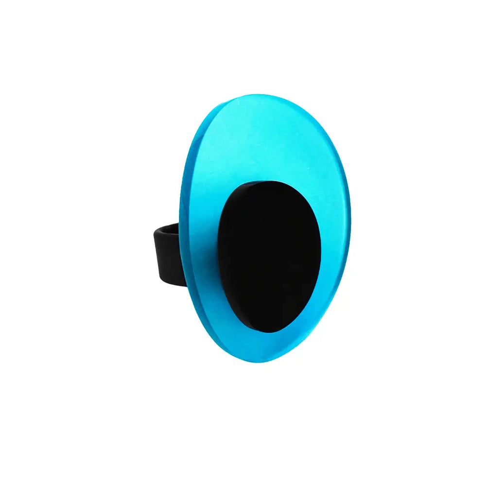 A round, blue, and black Leya Ring phone stand with a black grip from Alex + Svet. The Leya Ring has a vibrant blue top and appears to be extended. Reminiscent of the elegance found in modern jewelry, it adds flair to your phone. The background is plain white.