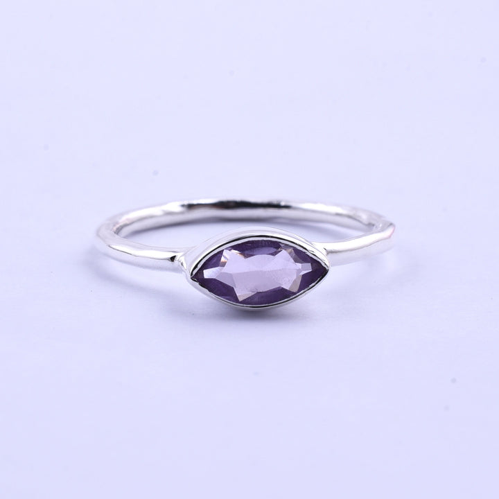 The Watermelon Tropical Silver Marquise Amethyst Ring features a delicate silver band with a marquise-cut amethyst at its center. The simple, elegant design showcases the gemstone's faceted surface set horizontally. A plain, light background accents the ring's intricate details perfectly.