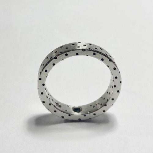 A **Fruit Bijoux Dots Ring** with a series of small black dots evenly distributed across its surface is standing upright, casting a slight shadow on a white background. The inner surface appears smooth, while the outer edge has a subtle star pattern.