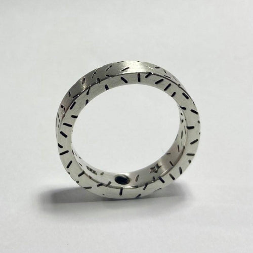 A Fruit Bijoux Dashes Ring with a matte finish and delicate, evenly spaced black engravings around its entire band. The background is a plain white surface, with the ring standing upright, casting a faint shadow.