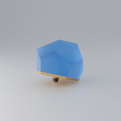 A geometric blue light fixture with a faceted design sits against a plain gray background. The fixture has a 24ct gold-plated base with a screw-in attachment at the bottom. Its polygonal shape and matte finish give it a modern and minimalist appearance: the Fruit Bijoux Fruit Bijoux Ring Top VU Crystals Sky Blue.