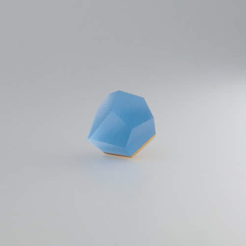 A geometric, multi-faceted object with a blue top and 24ct gold-plated bottom is displayed against a plain, white background. The Fruit Bijoux Ring Top VU Crystals Sky Blue by Fruit Bijoux has clean, sharp edges, and its design is minimalistic with a modern aesthetic.