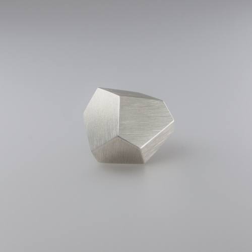 A small, uniquely shaped 925 sterling silver geometric object sits on a plain surface with a soft gradient background. Resembling exquisite handmade jewellery, the Fruit Bijoux Ring Top Goldrush from Fruit Bijoux features multiple flat, angled surfaces, giving it a faceted, modern appearance.