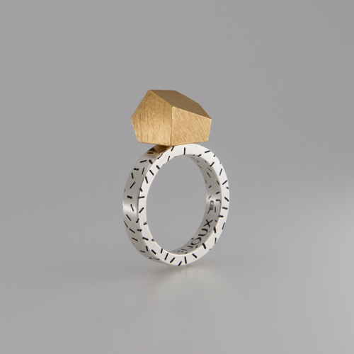 A modern geometric ring with a large, angular gold gemstone set on a 925 sterling silver band. The band is decorated with small, irregular black lines. The overall design, embracing a modular concept, is minimalist and contemporary. This exquisite piece is known as the Fruit Bijoux Ring Top Goldrush by Fruit Bijoux.