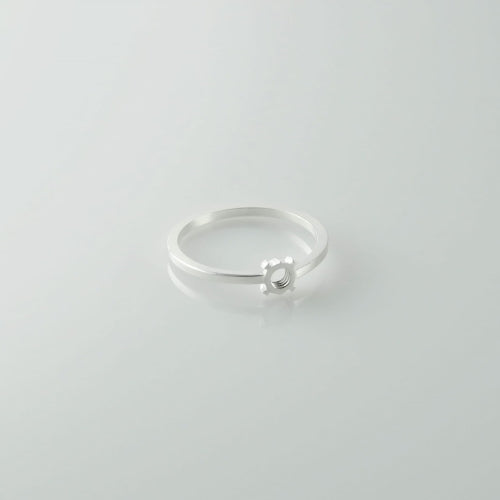 A minimalist sterling silver diamond ring with a thin band and a small circular diamond set in the center. This Fruit Bijoux Minimal Ring Silver by Fruit Bijoux tops off your look effortlessly, placed against a plain, light-colored background.