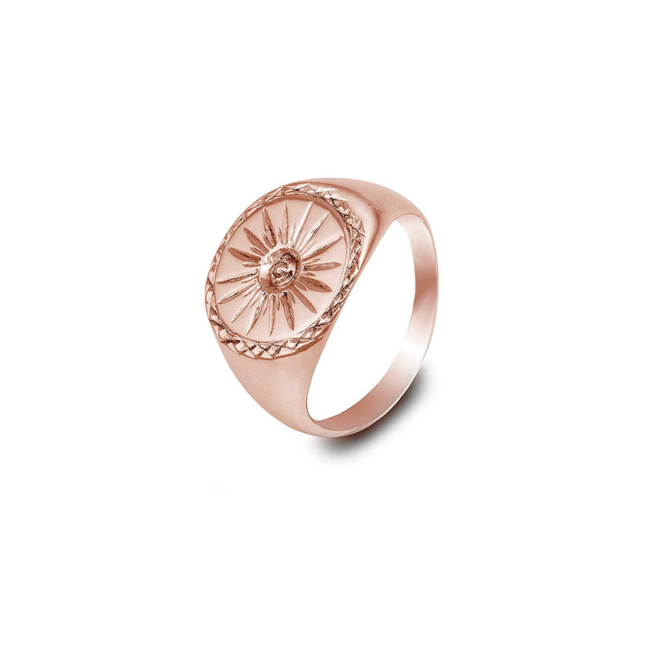 A Starburst 9ct Gold Signet Ring by Cosmic Boulevard featuring an engraved sunburst design on an oval-shaped face. The band is smooth and tapers towards the back. This handmade signet ring has detailed etchings around the sunburst, creating a textured border. The overall design is elegant and intricate.