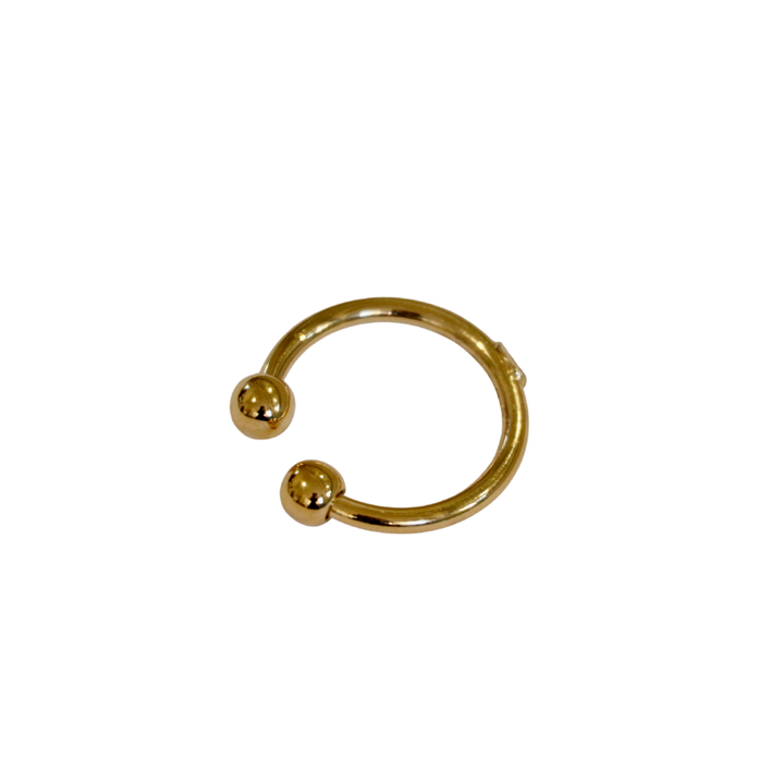 The Torque Ring in Gold Plated Brass by Zubeldia is a circular nose ring with golden balls on each open end, shown on a white background.