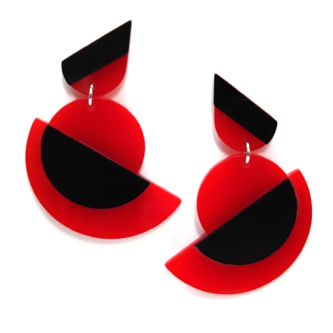 A pair of Suzanna statement acrylic earrings by Alex + Svet. Each earring has a small black and red triangle at the top, followed by a round red disc with a large black semi-circle overlay. Below the disc is a larger red half-circle. The design evokes Avant-Garde aesthetics and is modern and abstract.