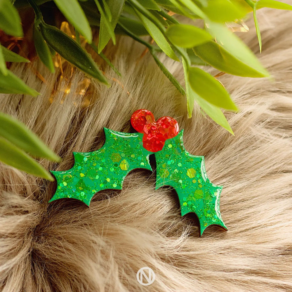 The Naoi Holly Pin Brooch is a festive wooden accessory with two glittery green leaves and three red berries, perfect for adding holiday cheer to any outfit.
