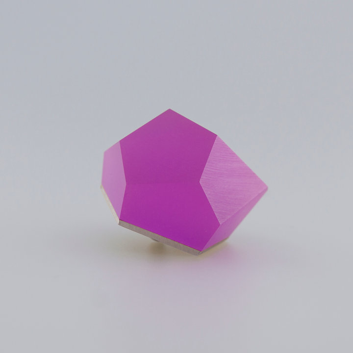 A smooth, multifaceted Fruit Bijoux Ring Top VU Crystals Magenta Pink with sharp edges and a shiny surface set atop a 24ct gold-plated ring against a plain white background by Fruit Bijoux.