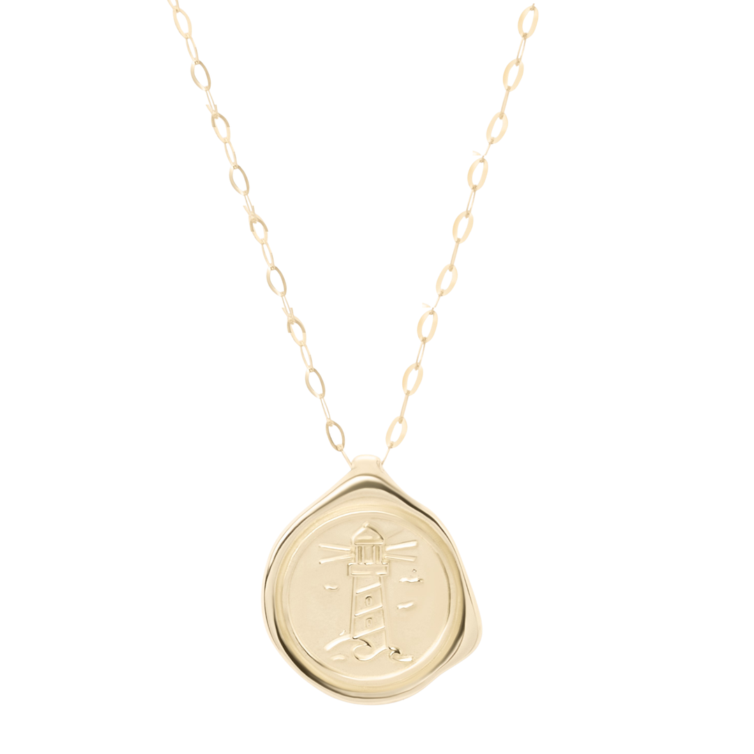 The 9ct Gold My Guiding Light Pendant by Ava Jane Jewellery features a delicate chain and a round, wax seal-style 9ct gold pendant engraved with a lighthouse, birds, and rays of light, finished with an organic edge for handcrafted Dublin charm.