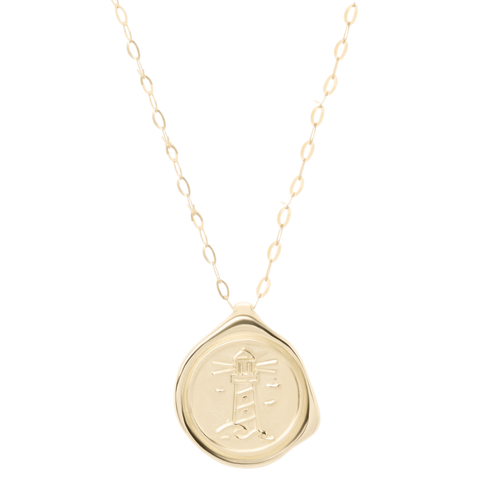 The 9ct Gold My Guiding Light Pendant by Ava Jane Jewellery features a delicate chain and a round, wax seal-style 9ct gold pendant engraved with a lighthouse, birds, and rays of light, finished with an organic edge for handcrafted Dublin charm.