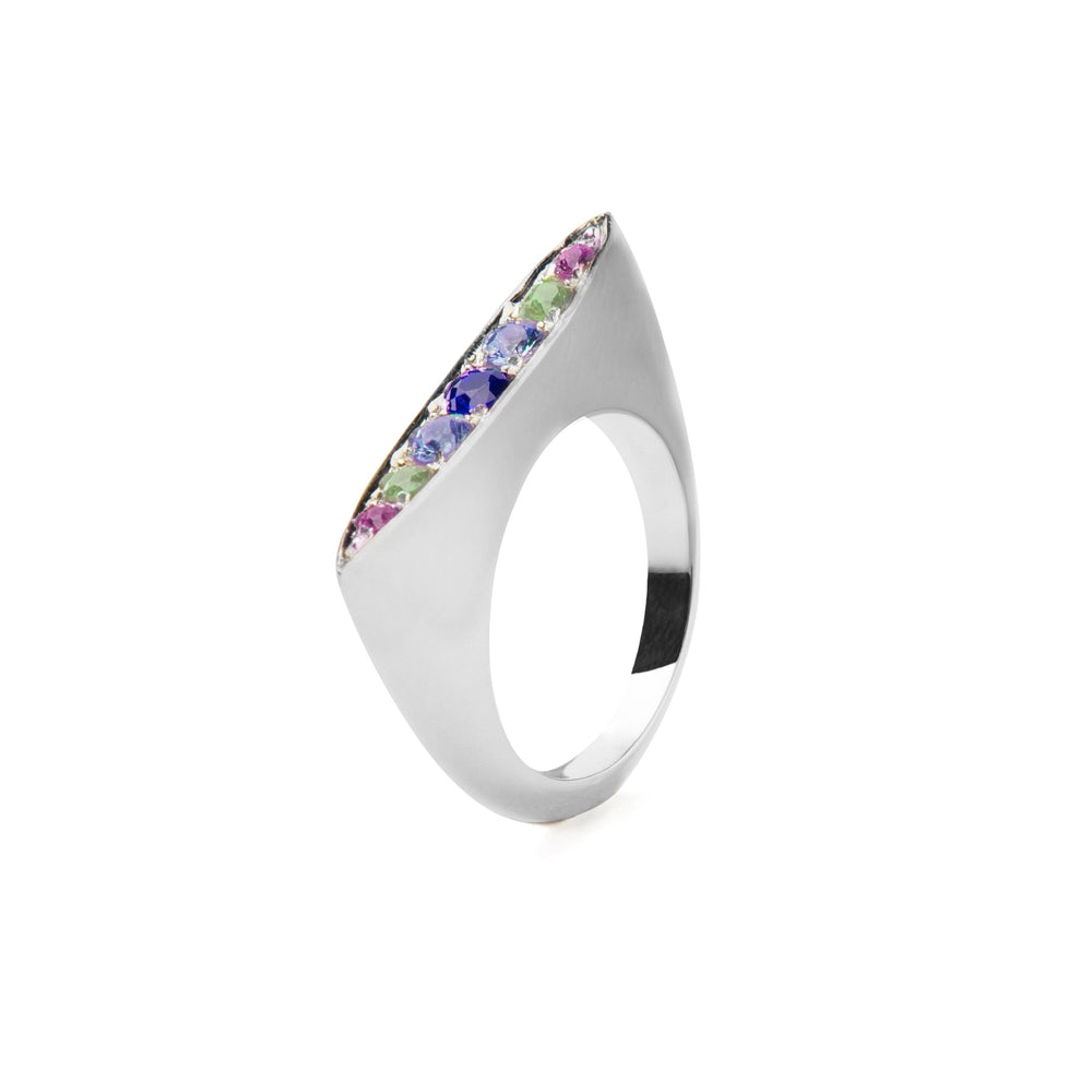 A sterling silver ring with a sleek, modern design, featuring a narrow, elongated top encrusted with small gemstones in shades of blue, green, and purple sapphires arranged in a row. The **Eveningstar Sapphire Ring** by **Cosmic Boulevard** is isolated on a white background.